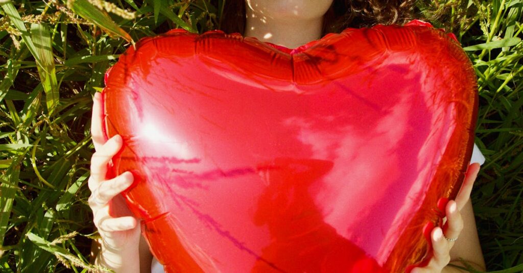 Young woman relaxing outdoors while holding a vibrant red heart-shaped balloon, evoking warmth and romance.